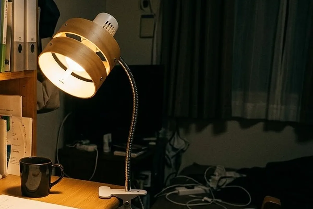 夜の机の天板の縁に白いクリップで留めたクリップライト。木のリングの笠から電球の光が机のマグカップを照らしている