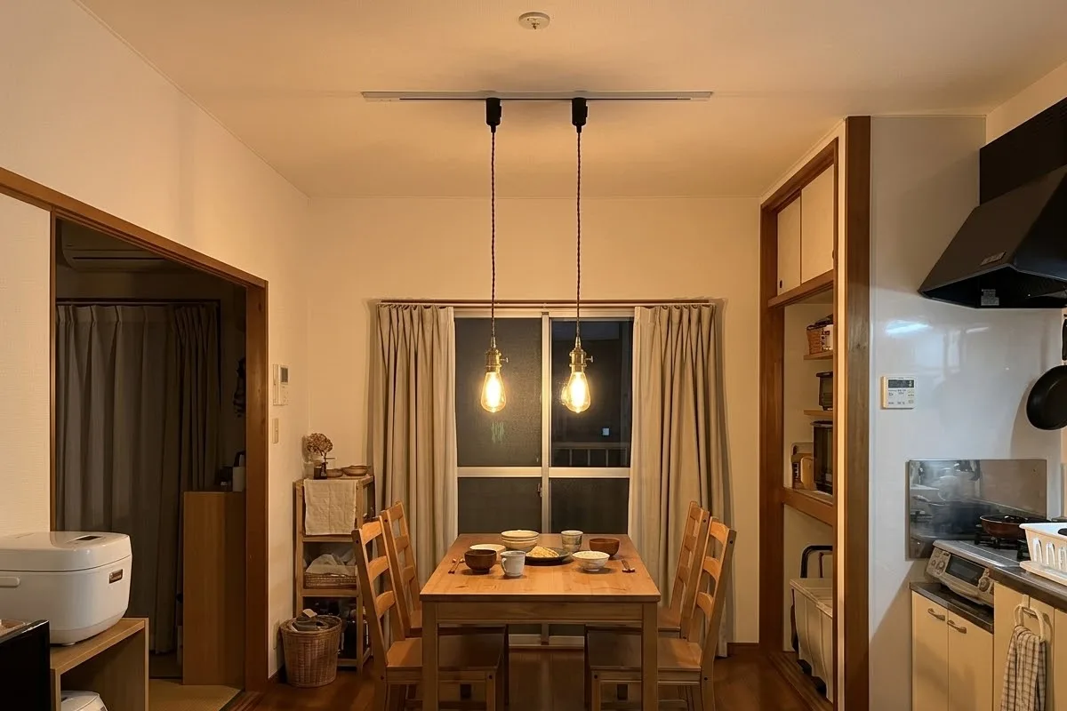 夕方の食卓。天井の白いダクトレールから、真鍮のソケットに電球を付けたペンダントライトが2つ、テーブルの上に下がっている